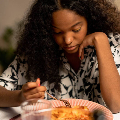 Woman looking down at her meal with a thoughtful, uncertain expression, wondering how the food will affect her body