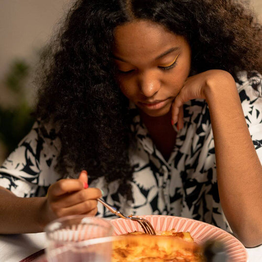 Woman looking down at her meal with a thoughtful, uncertain expression, wondering how the food will affect her body